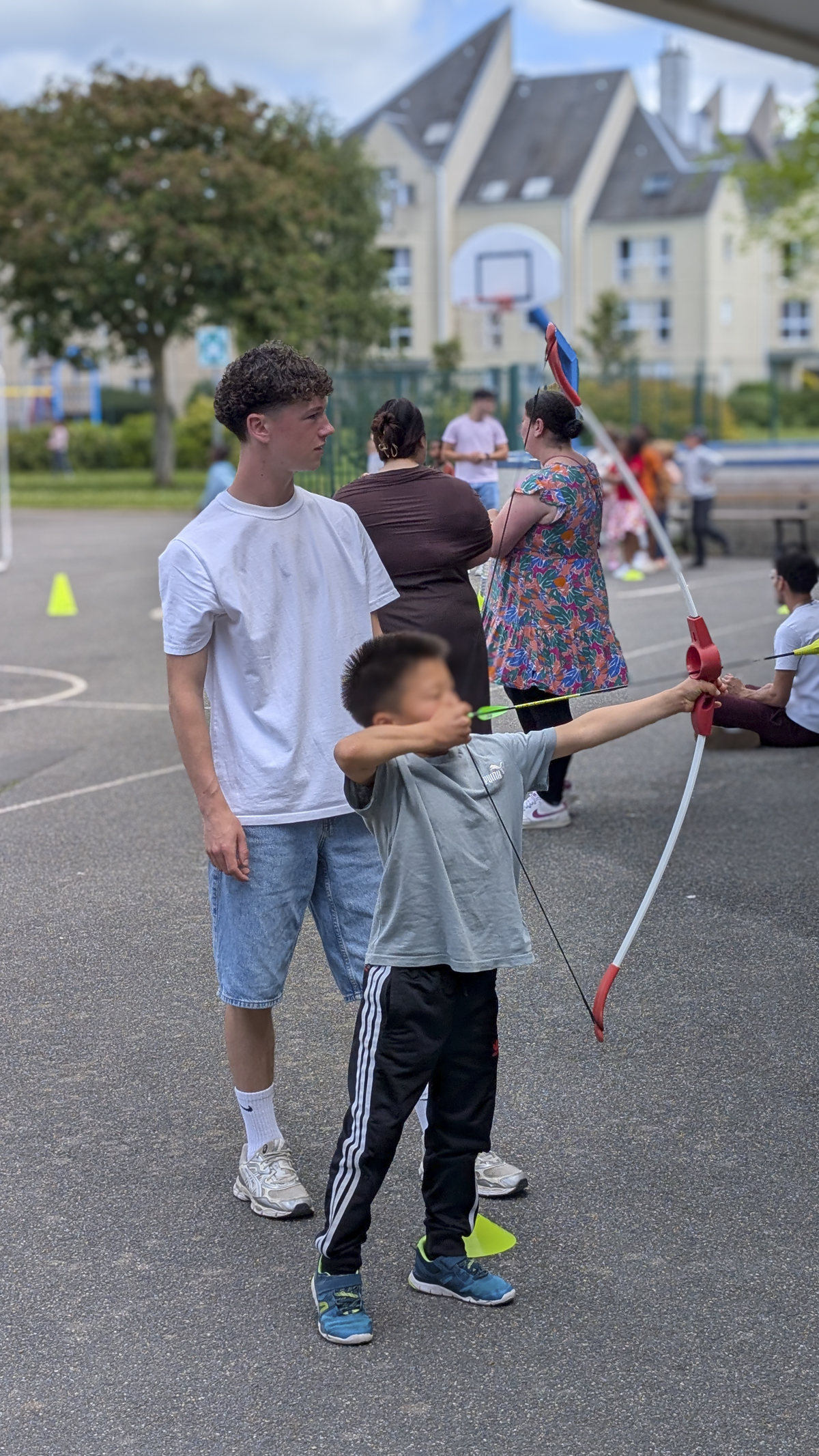 un étudiant de L3 ES avec un enfant qui fait du tir à l'arc dans une cours d'école